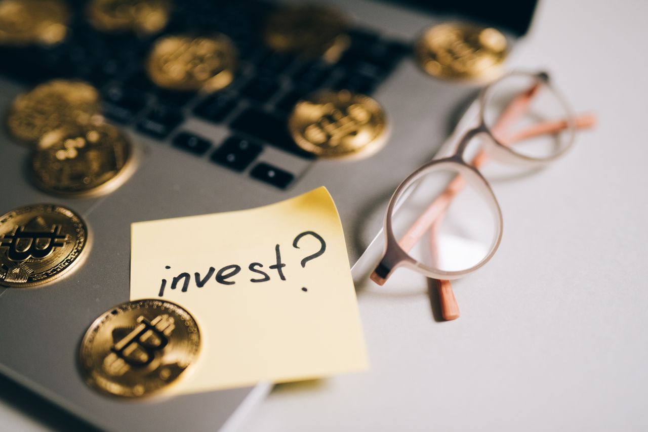 The Art of Drawing Readers In: Your attractive post title goes here A close-up of bitcoin coins on a laptop with eyeglasses and a sticky note reading 'invest?'